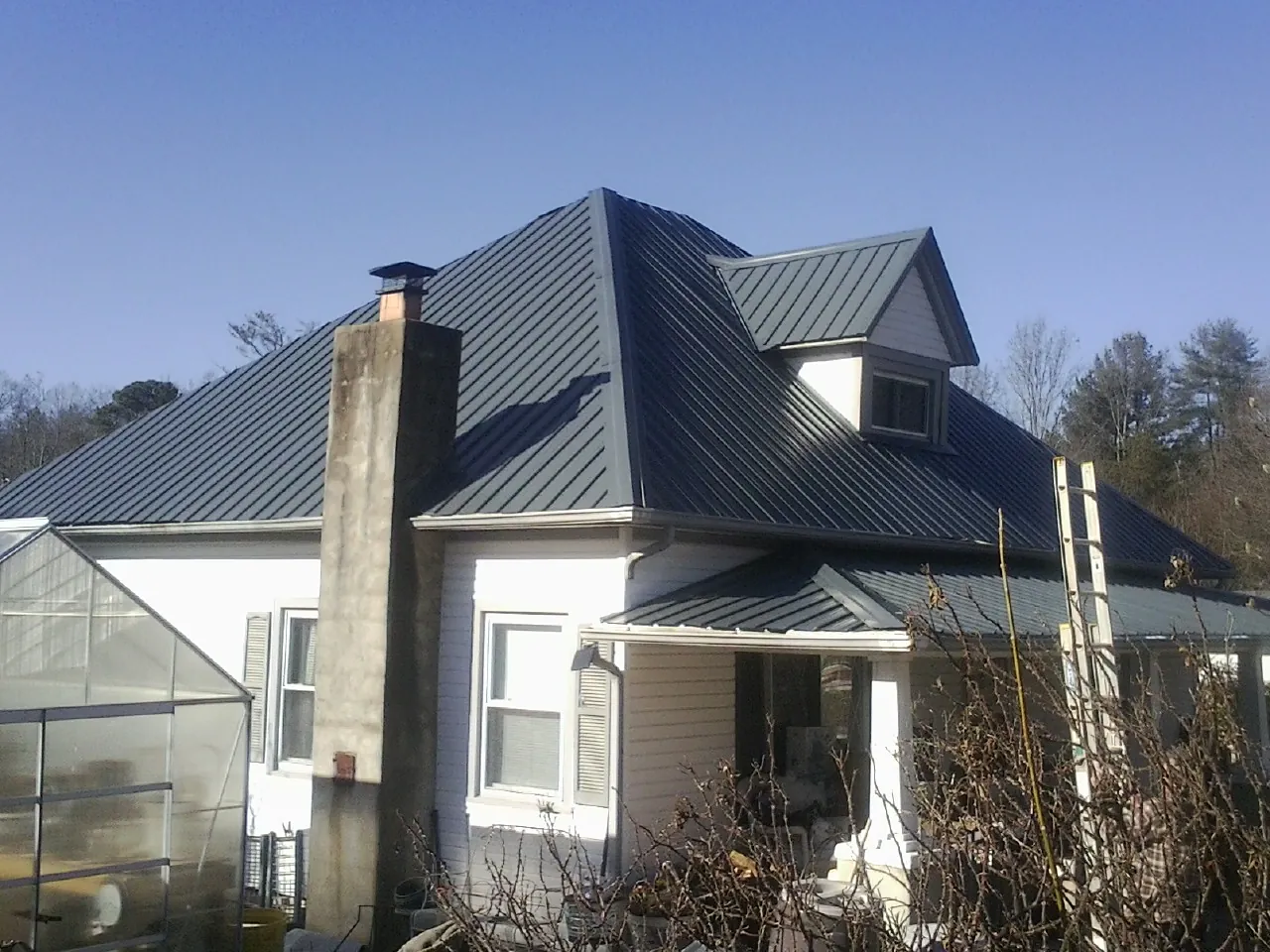Dark blue standing seam metal roof on a white farmhouse with dormer — Slate & Tile Roof Repair by Roofing Brothers in Posen