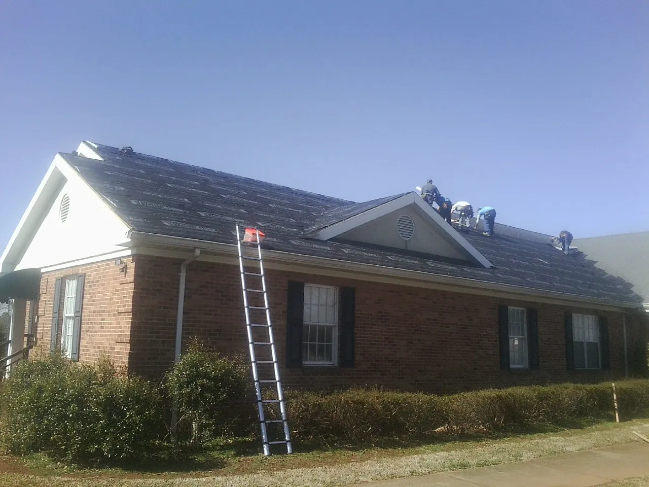 Crew tearing shingles off a brick ranch roof with a ladder set — Emergency Roof Repair work by our crew in Posen
