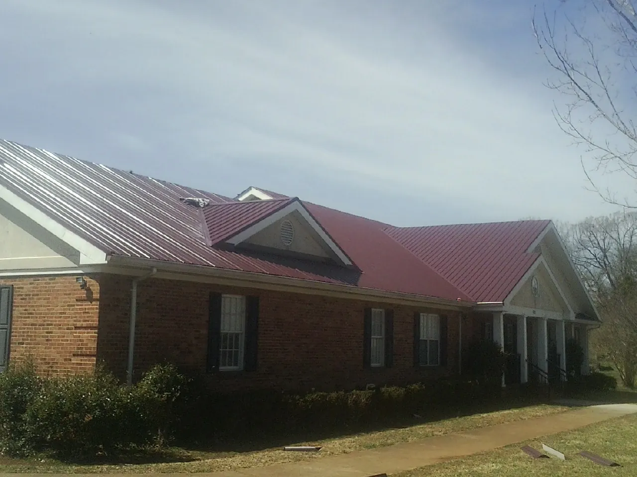 Red metal roof with gabled entries on a long brick building, from a Hail Damage Roof Repair job in Posen