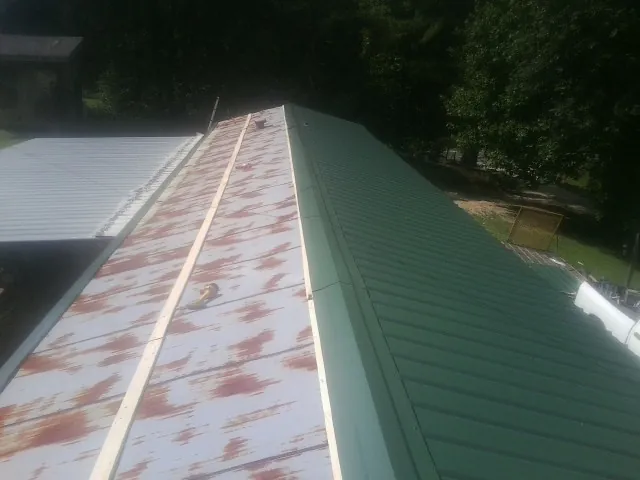Old rusted panels beside newly installed green metal roofing — Wind Damage Roof Repair by Roofing Brothers in Posen