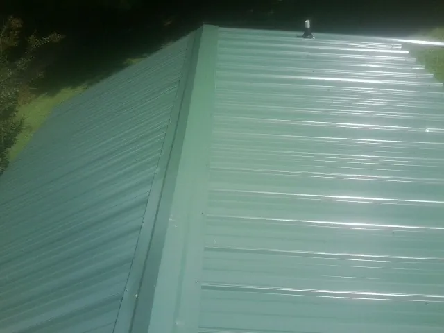 New green metal panels meeting at the ridge of a roof — Flat Roof Repair work by our crew in Posen