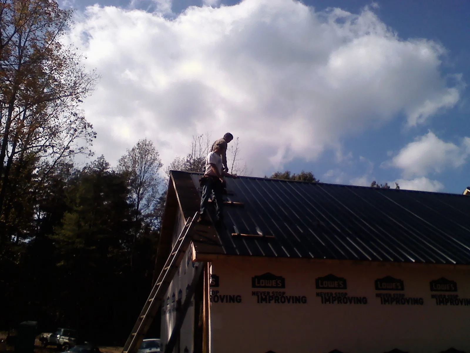Roofer fastening dark metal panels high against a cloudy sky, from a Roof Inspection job in Posen