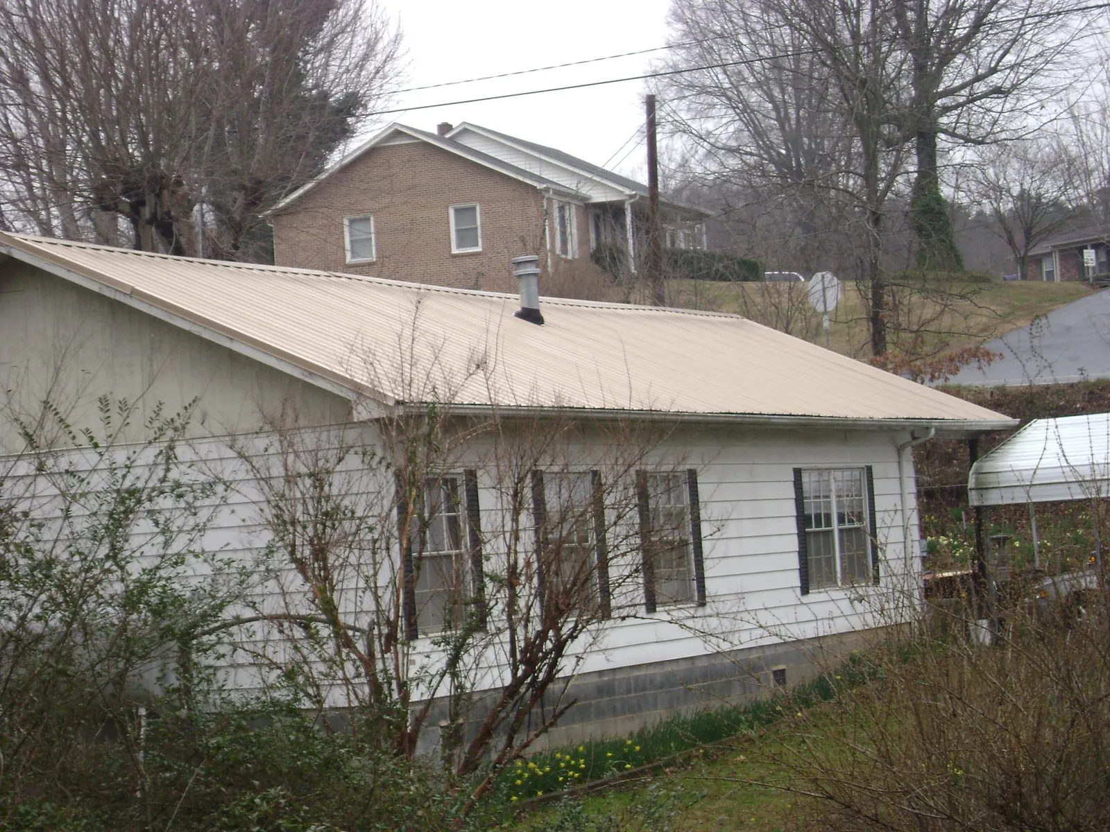 Tan metal roof on a white sided house set into a hillside — Commercial Roofing by Roofing Brothers in Posen